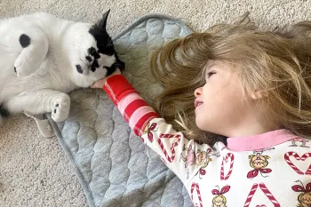 A young girl laying on the floor caresses her pet cat who contentedly leans into her hand