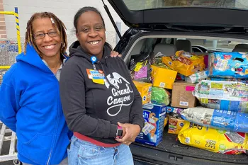 Two women standing in front of their car trunk full of pet food donations