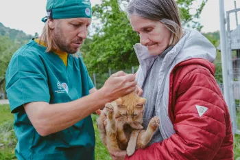 A woman holds a cat while a vet checks them over