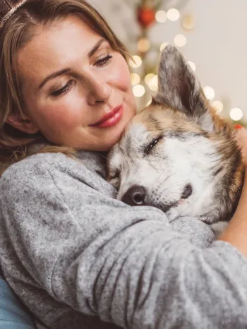 Woman and her dog cuddling on the couch with holiday lights behind them